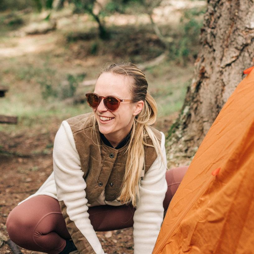 Woman in sunglasses and outdoor attire sitting next to a tree