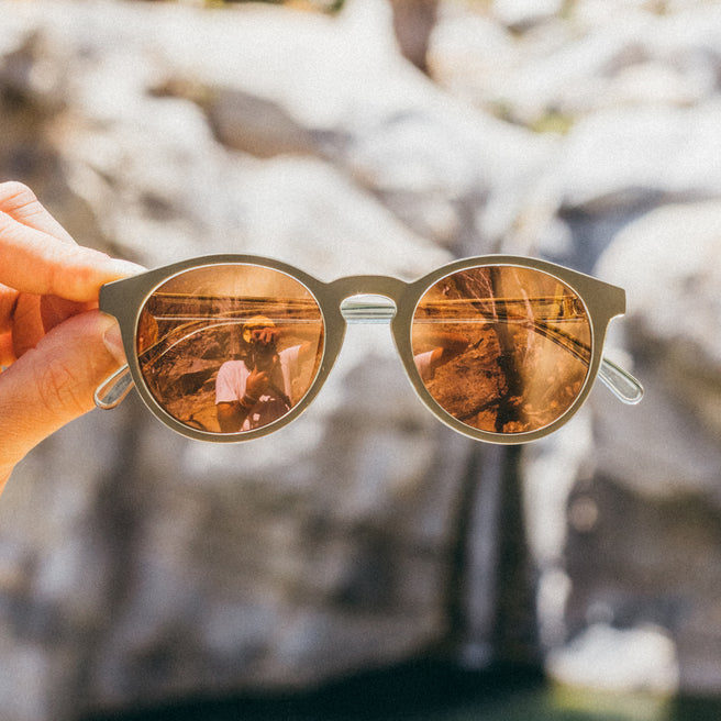 Sunglasses with reflective lenses held against a natural background