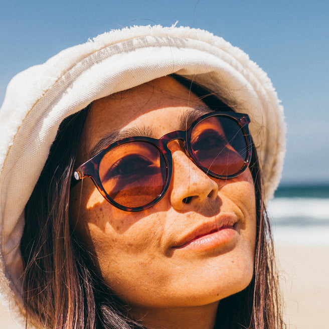 Woman wearing sunglasses and a hooded towel on a beach