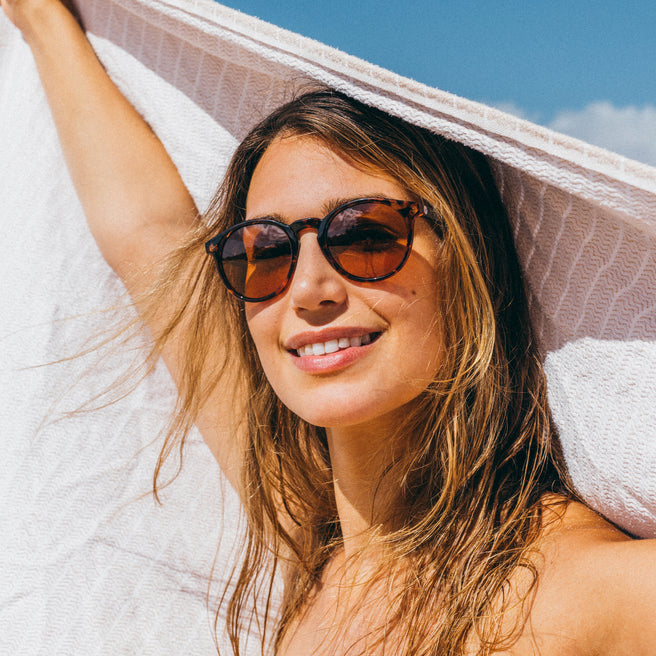 Woman wearing sunglasses and a white towel, enjoying the sun.