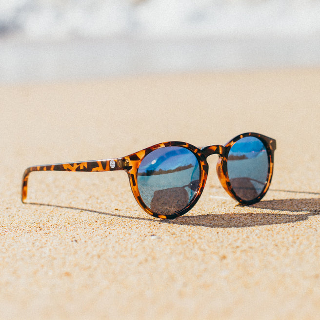 Sunglasses with tortoiseshell frame and blue lenses on a sandy surface