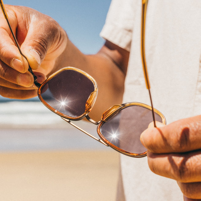 Estero - Horizon Slate - Person holding a pair of sunglasses with a blurred background