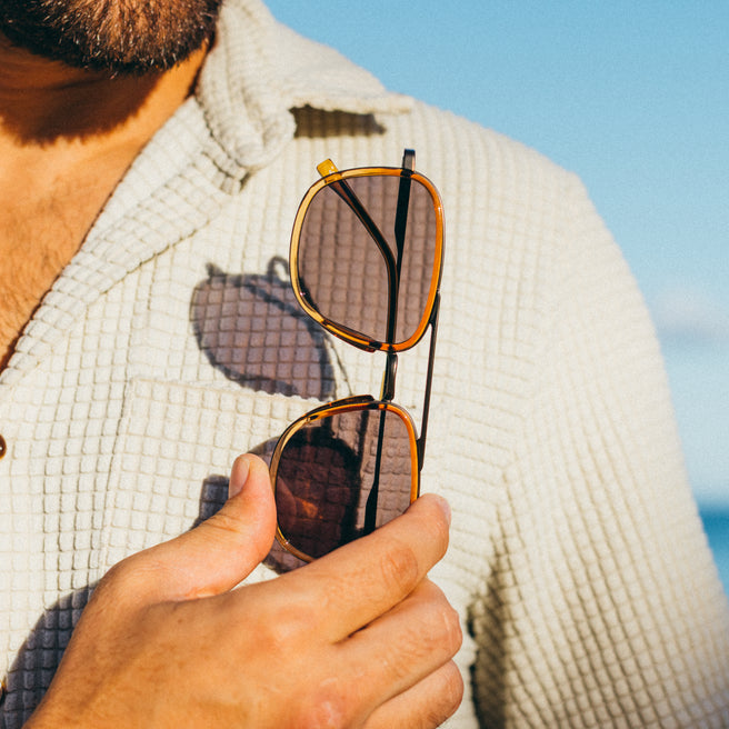 Estero - Horizon Slate - Person holding sunglasses with a blurred background