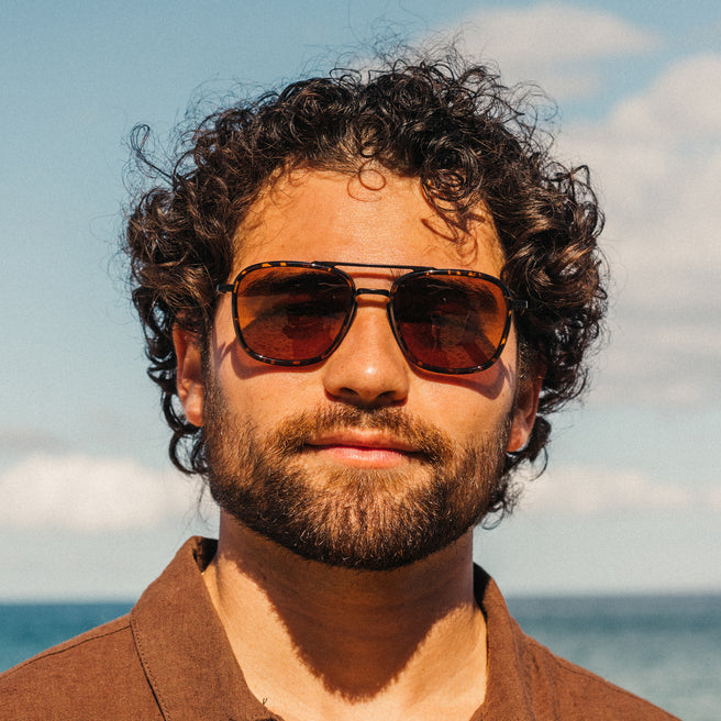 Man wearing sunglasses with a beach and sky background