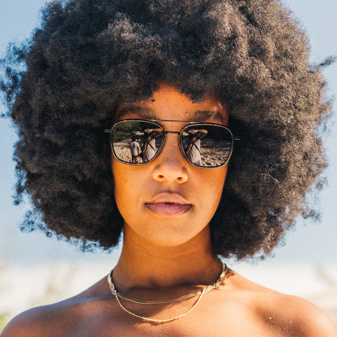 Person with an afro wearing sunglasses against a blurred natural background