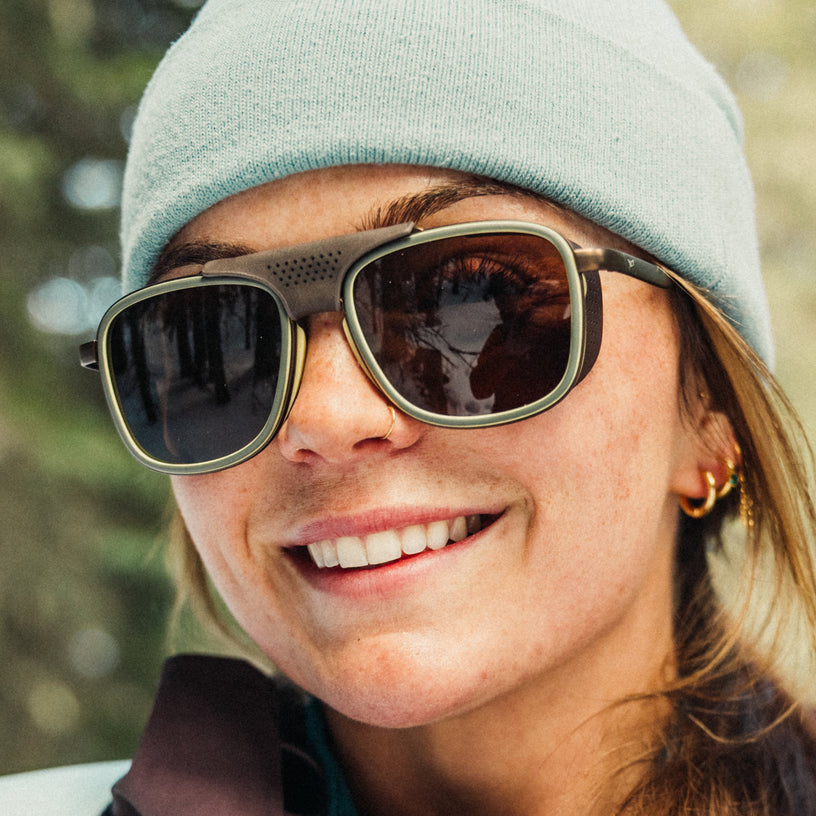 Person wearing sunglasses and a beanie with a blurred natural background