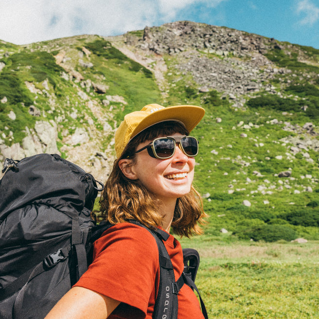 Ferrata - Olive Citrine Amber - Person with a backpack and sunglasses standing in a mountainous landscape