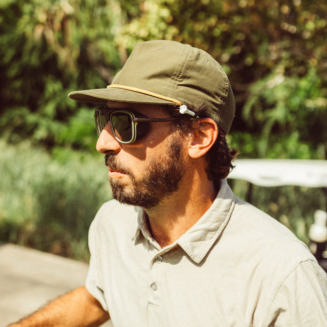 Ferrata - Olive Citrine Amber - Man wearing a green cap and sunglasses with a blurred natural background
