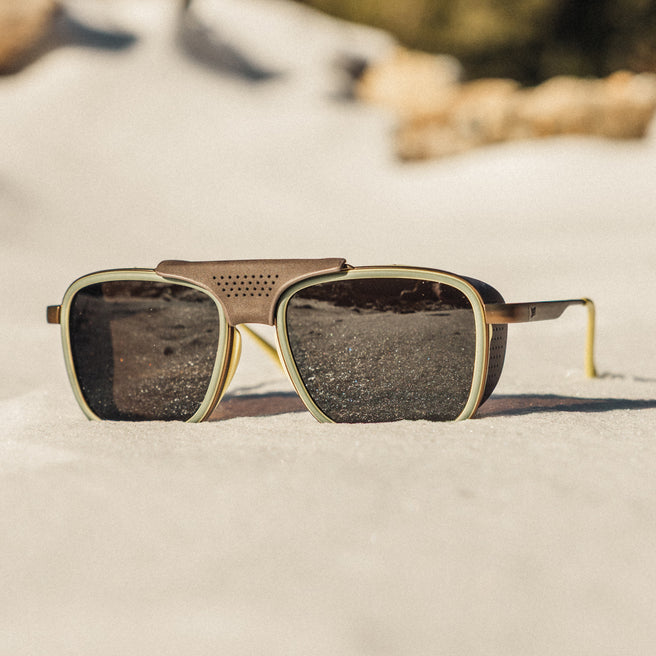 Sunglasses with gold frame and dark lenses on a sandy surface