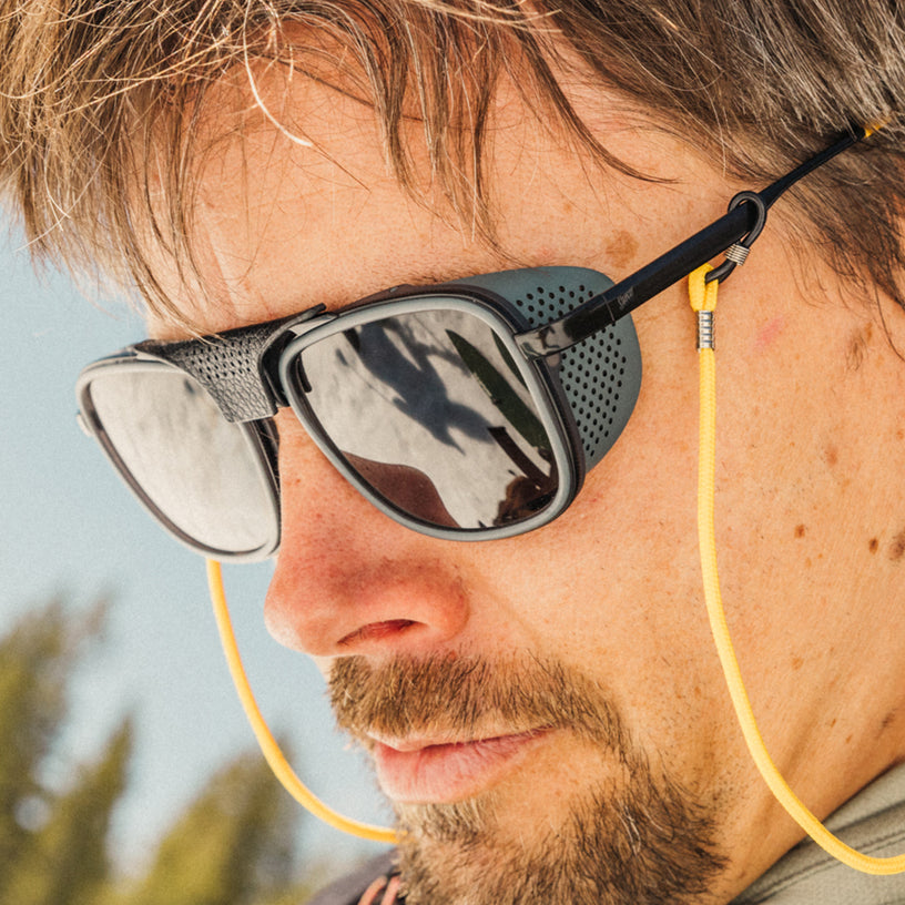 Man wearing sunglasses with a yellow cord, outdoor setting