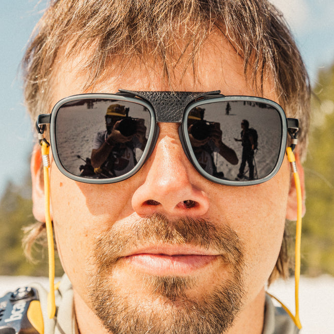Close-up of a person wearing reflective sunglasses with a blurred outdoor background