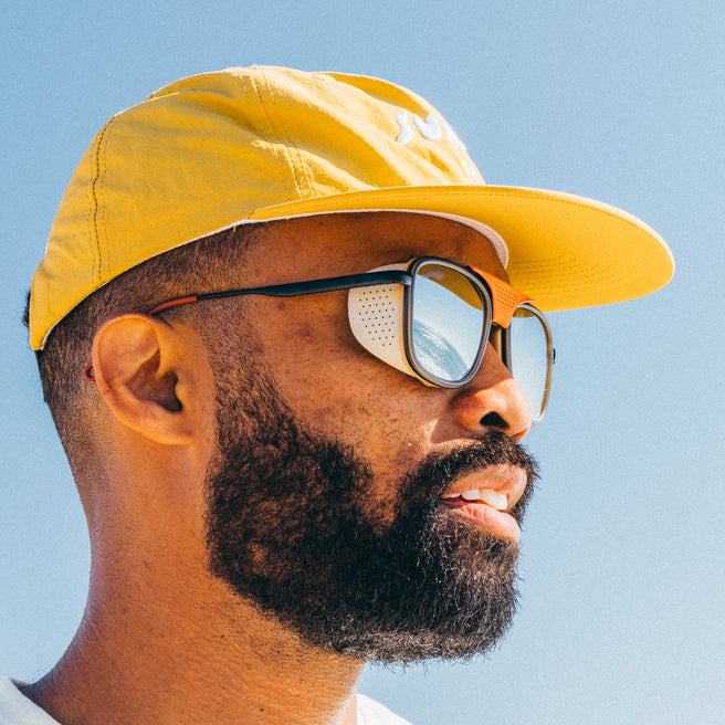 Man wearing a yellow cap and reflective sunglasses against a clear blue sky