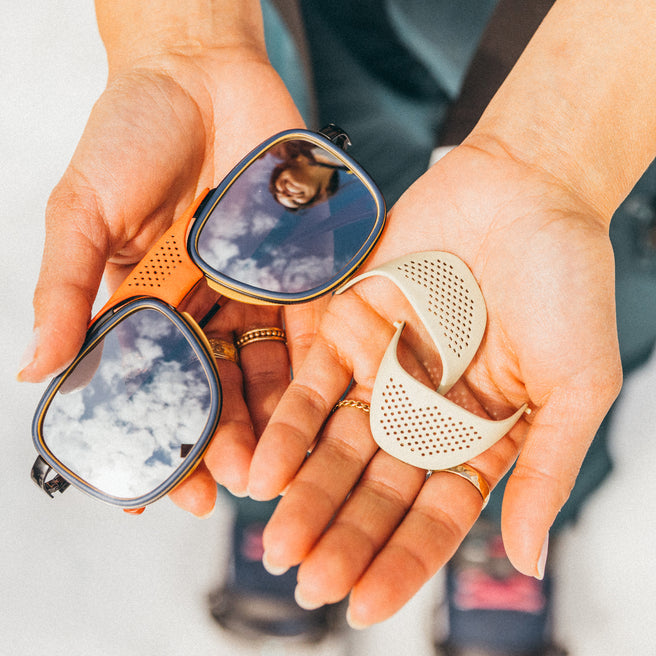 Person holding sunglasses with reflective lenses and a small tool in their hands.