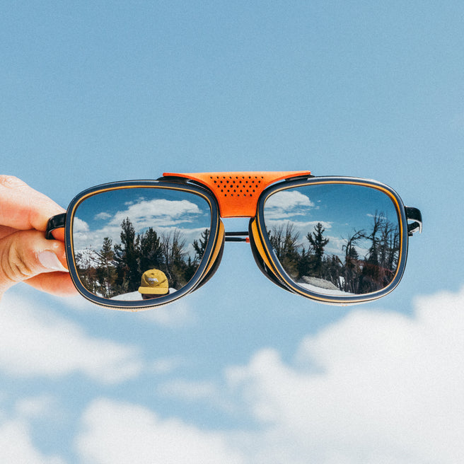 Sunglasses held up with a snowy landscape reflection on a clear blue sky background