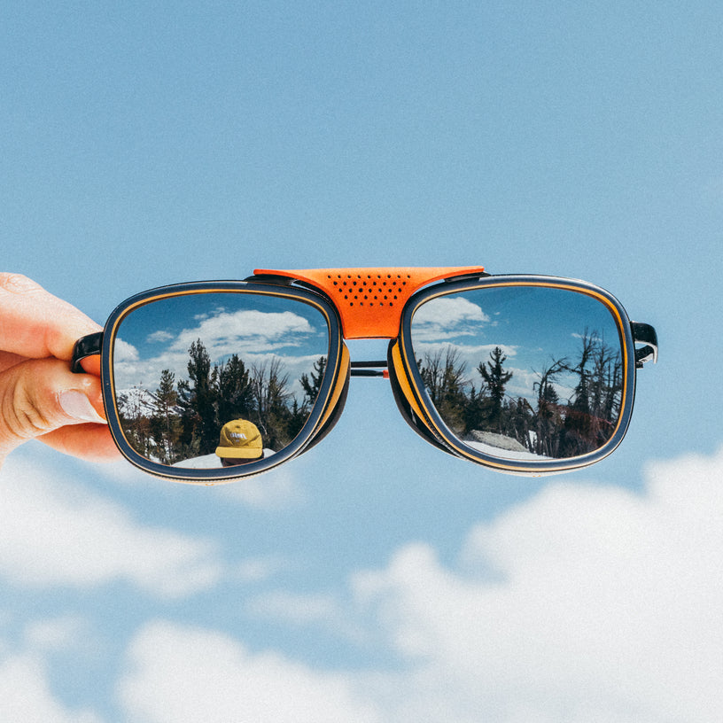 Sunglasses held up with a snowy landscape reflection on a clear blue sky background