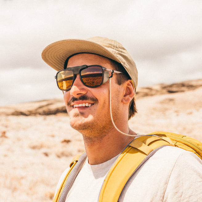 Ferrata - Tortoise Bronze - Man wearing a hat and sunglasses with a yellow backpack in a desert setting