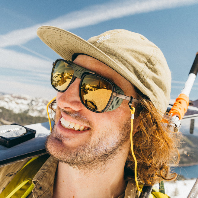 Man wearing a beige hat and sunglasses with a snowy landscape in the background
