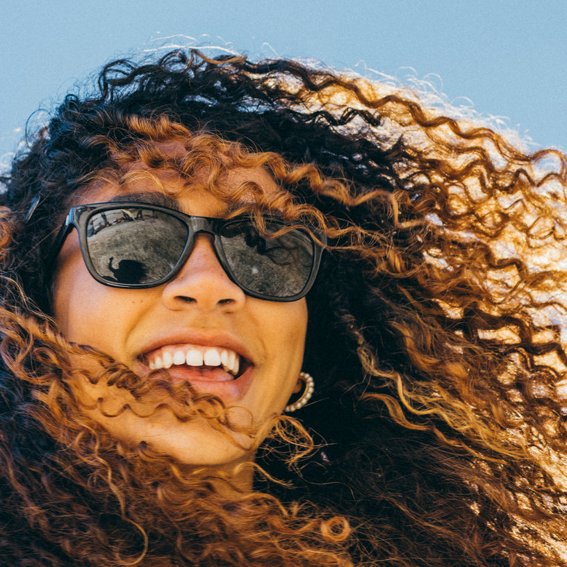 Person with curly hair wearing sunglasses against a blue sky