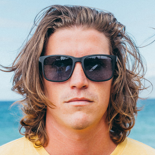 Man with sunglasses and long hair against a blue sky background