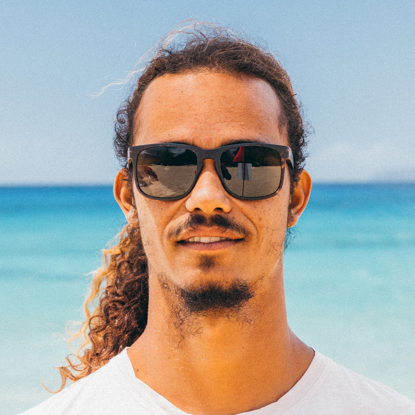 Man wearing sunglasses with a beach and blue sky in the background
