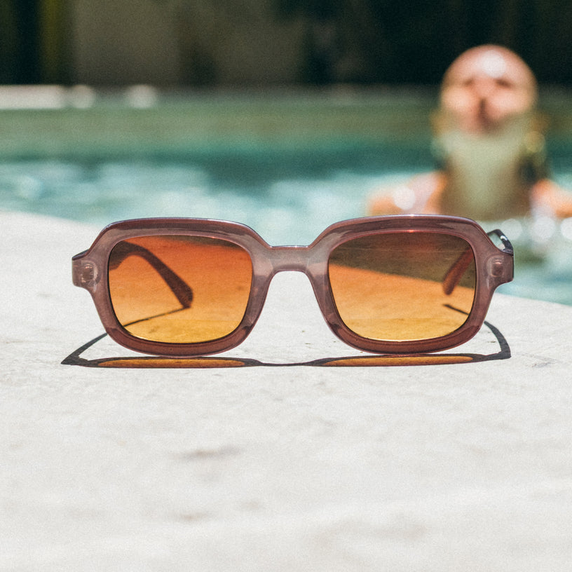Sunglasses with orange lenses on a white surface with a blurred pool background