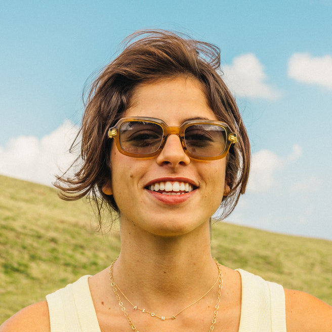 Woman wearing sunglasses with a scenic background of a field and blue sky.