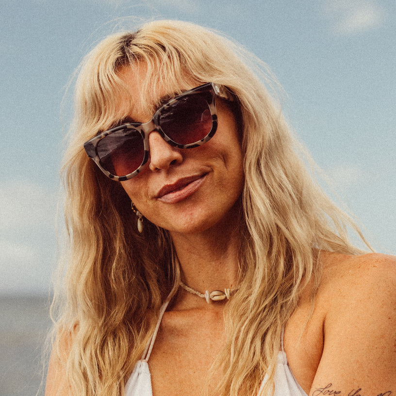 Woman with sunglasses and blonde hair against a blue sky.