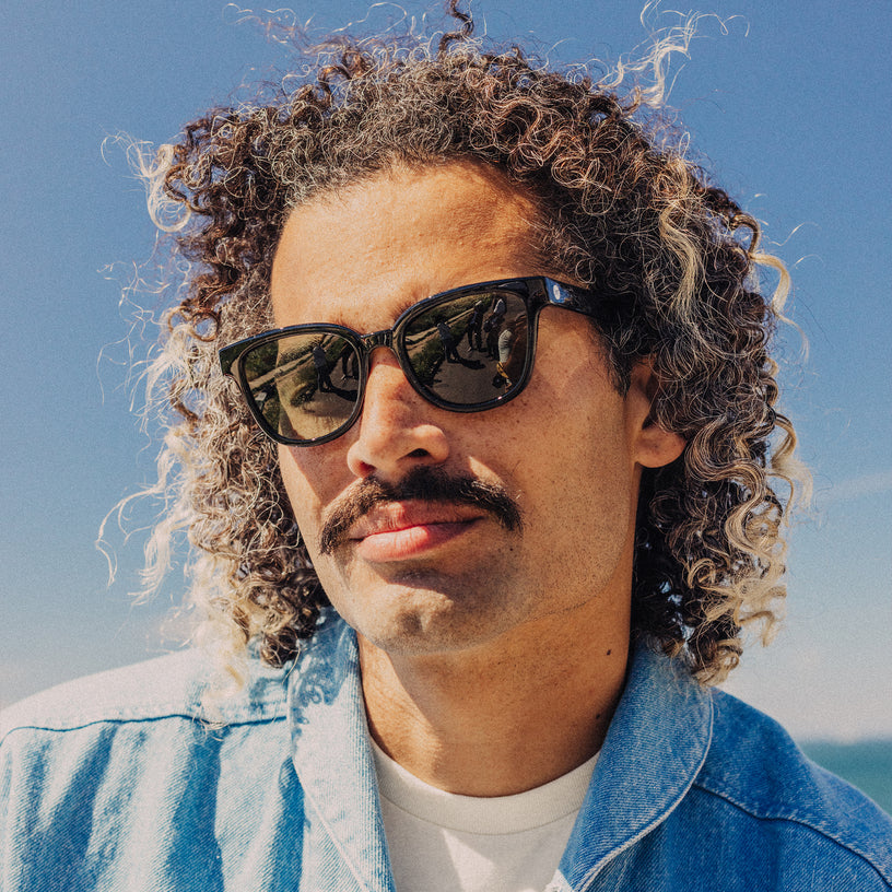 Man wearing sunglasses and a denim jacket with a clear blue sky background