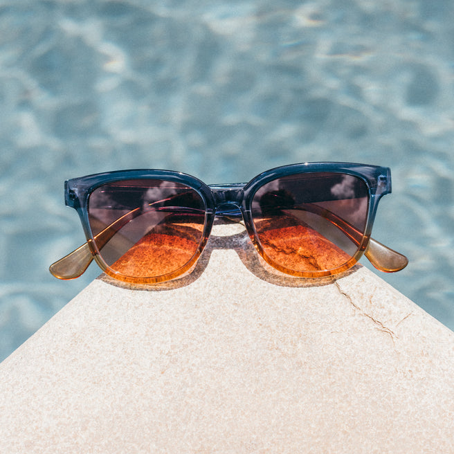 Sunglasses with orange lenses on a stone ledge by a pool