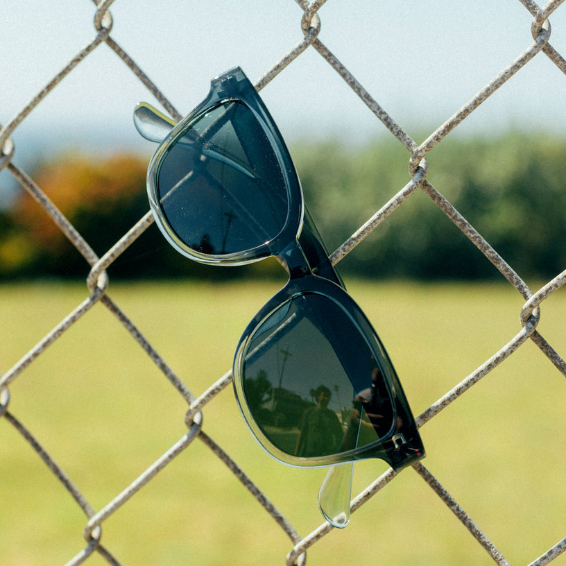 Black sunglasses with reflective lenses on a chain-link fence with a blurred outdoor background