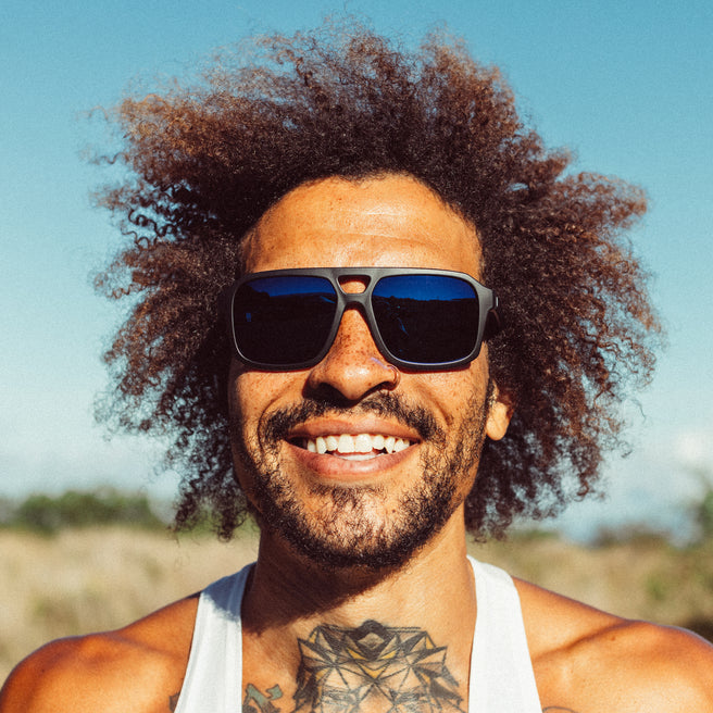 Man with sunglasses and curly hair smiling outdoors