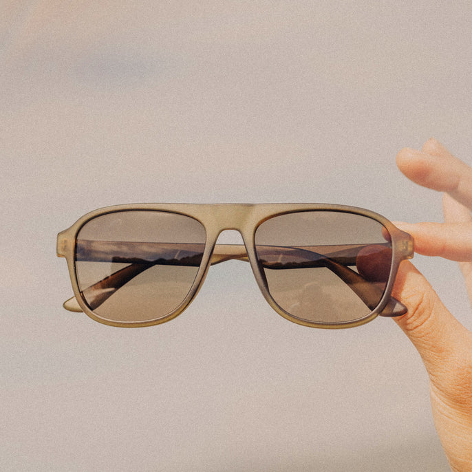 Sunglasses held by a hand against a plain background