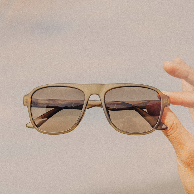 Sunglasses held by a hand against a plain background