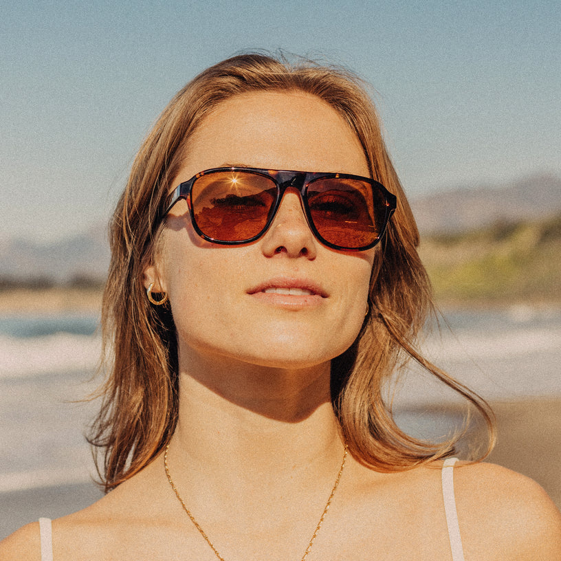 Woman wearing sunglasses with a beach and ocean in the background