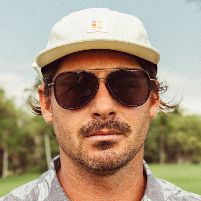 Man wearing sunglasses and a cap outdoors with trees in the background