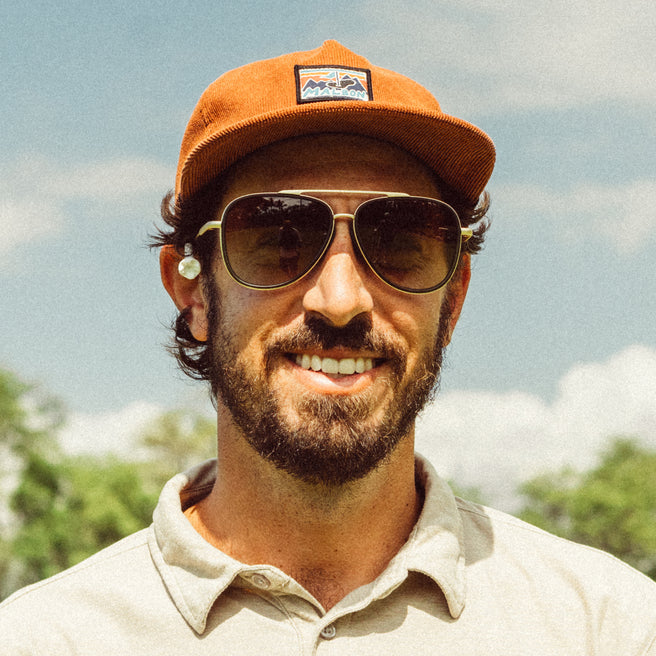 Man wearing a brown cap and sunglasses with a blurred natural background