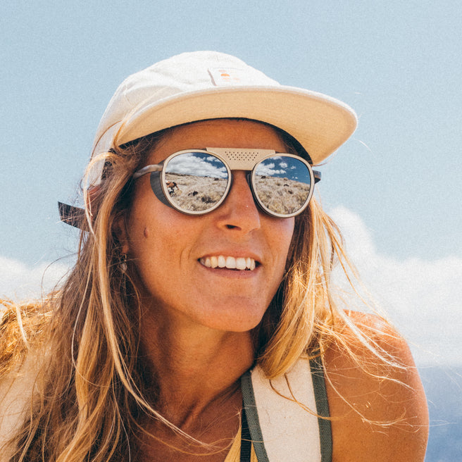 Person wearing a beige cap and sunglasses with a clear blue sky background