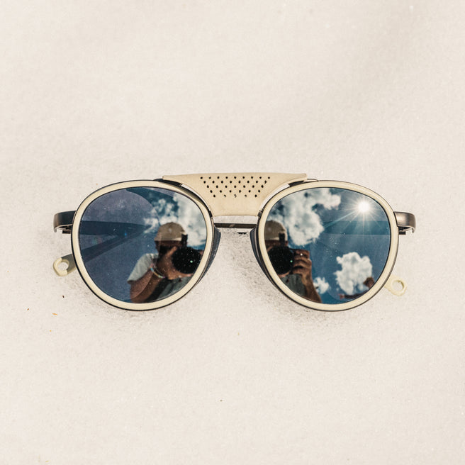 Strada - Ivory Silver - Sunglasses with reflective lenses showing a blue sky and clouds on a beige background