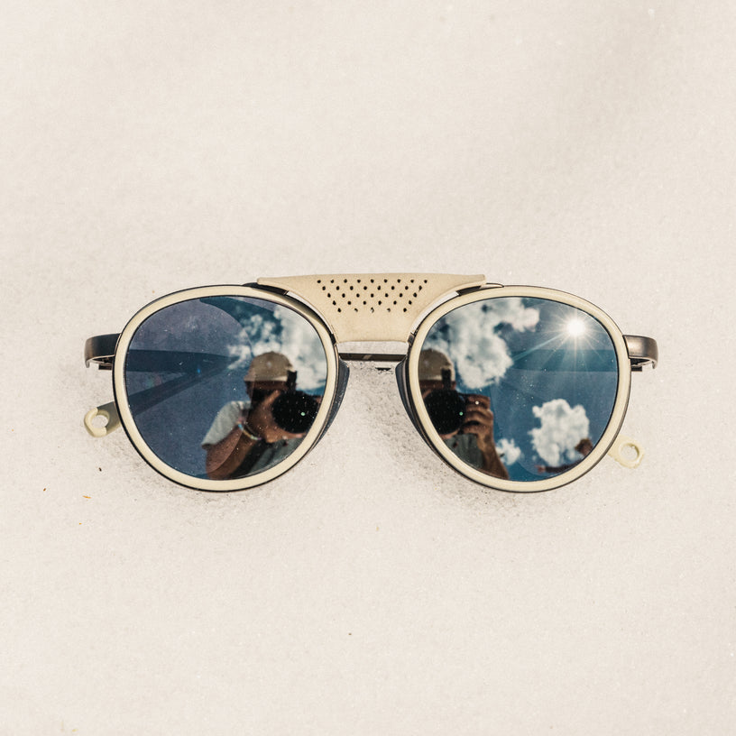 Sunglasses with reflective lenses showing a blue sky and clouds on a beige background
