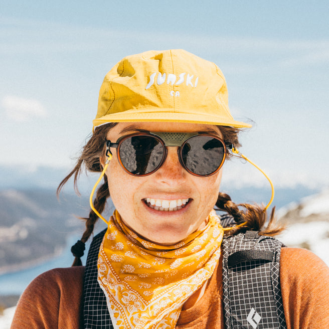 Strada - Rust Amber - Person wearing a yellow cap and sunglasses with a mountainous background