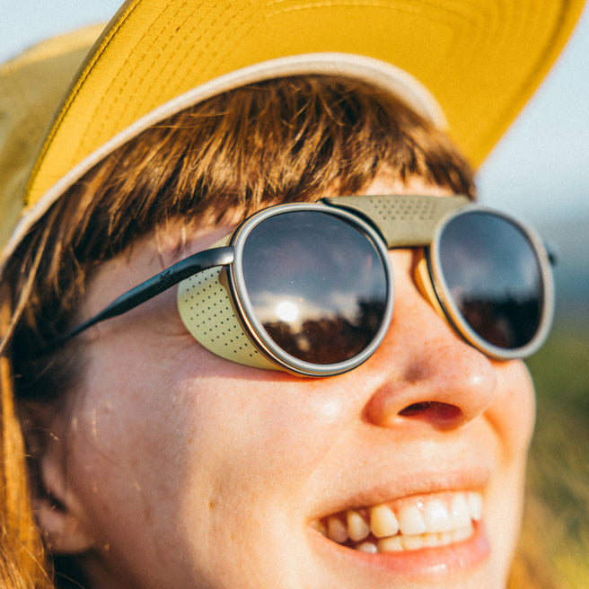 Strada - Sand Amber - Person wearing a yellow cap and round sunglasses with a blurred natural background