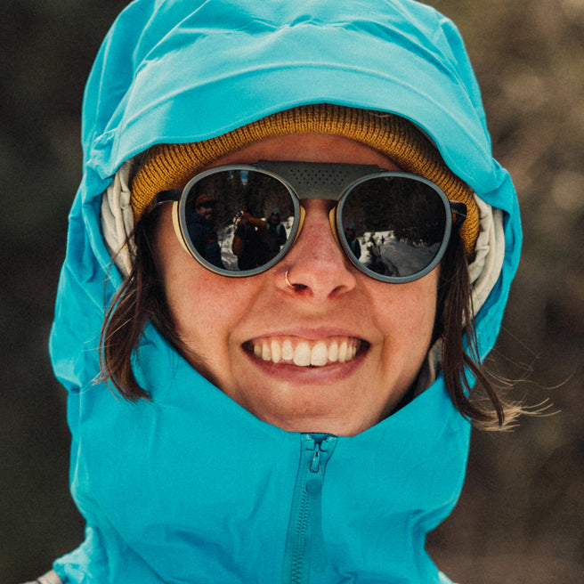 Person wearing a blue hooded jacket and sunglasses with a blurred background