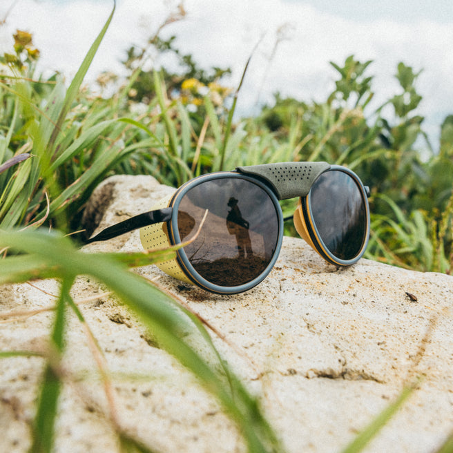 Strada - Sand Amber - Sunglasses with green strap on a rock surrounded by grass and plants