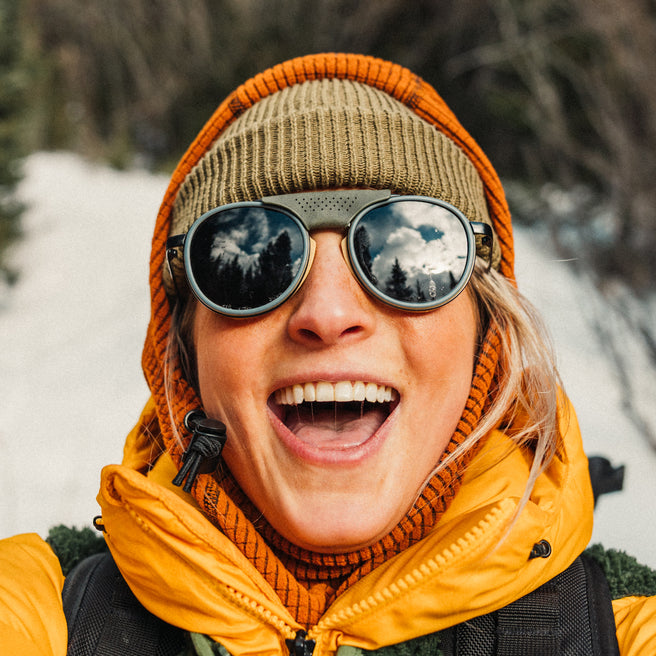 Person wearing a yellow jacket, orange beanie, and reflective goggles with a snowy background