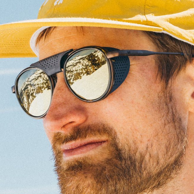Close-up of a person wearing sunglasses and a yellow hat with a blue sky background