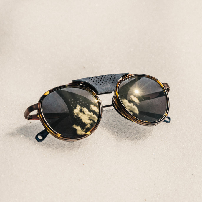 Round sunglasses with reflective lenses on a sandy background