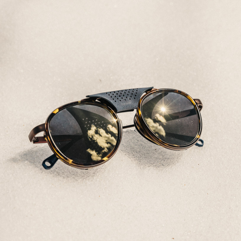 Round sunglasses with reflective lenses on a sandy background