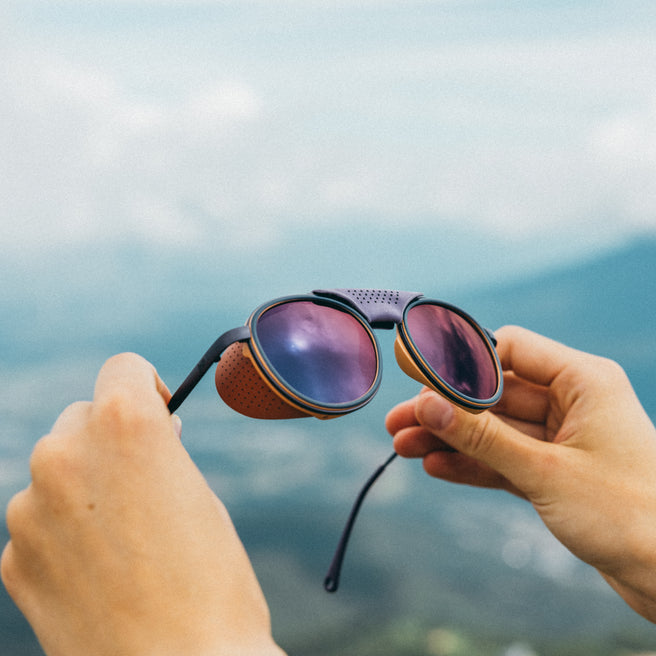 Strada - Violet Galaxy - Sunglasses with purple lenses held by hands against a blurred natural background