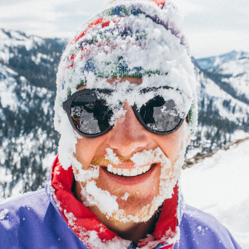 Person with snow-covered face and goggles in a snowy mountain landscape