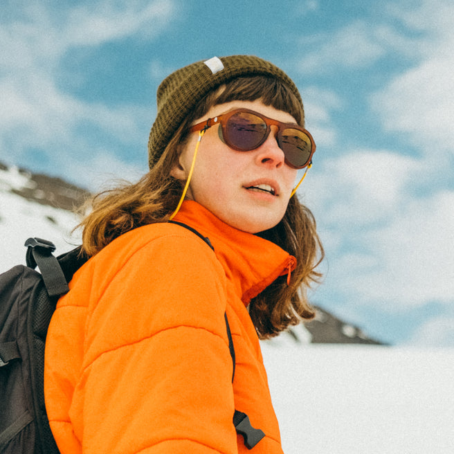 Person wearing an orange jacket and sunglasses with a snowy landscape in the background